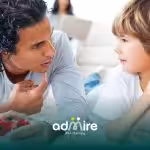 A therapist and autistic boy lying on a carpet holding video game controllers and making eye contact during playtime.