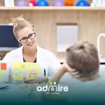 Female therapist showing colorful shape cards to a young autistic boy during an educational therapy session.