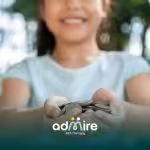 Smiling autistic child holding out coins with both hands outdoors, symbolizing savings or financial support.