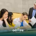 A male therapist observes ABA therapy students writing an exam in a lecture hall classroom environment.