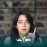 A Female therapist raises her index finger with a thoughtful expression, standing in front of a bookshelf background.