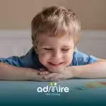 Happy autistic child smiling at their artwork on a table, reflecting confidence, creativity, and positive reinforcement.