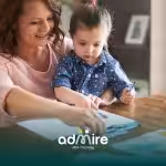 Therapist supports autistic toddler in a home drawing activity, building fine motor skills, focus, and early learning.