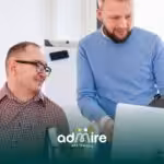 Two therapists collaborating at a desk with a laptop and clipboard, representing supportive workplaces and teamwork.