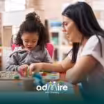 Therapist helping an autistic girl with a learning puzzle at a classroom table, representing early education & therapy.