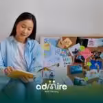 An ABA therapist sitting in front of a vision board filled with personal goals, inspirations, & memories, reading a notebook.