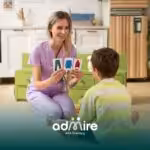 A therapist and autistic boy play a matching game with visual cards, working on building cognitive skills in a cozy home.