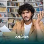 Confused ABA student sitting in a library looking at paperwork with raised hand, appearing frustrated.