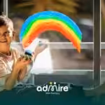 Autistic child sitting by a window painting a colorful rainbow on glass with bright paints during a creative art activity.