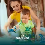 Therapist and autistic toddler painting together on floor, showcasing sensory play and early ABA therapy techniques.
