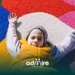 Autistic boy lying on colorful playground surface with arms stretched out, engaging sensory input and outdoor play activity
