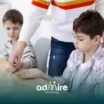 Therapist giving a supplement or medication to an autistic boy at the table while another autistic child sits nearby.