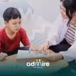 Therapist working with autistic boy on drawing activity at table, supporting communication, learning, and fine motor skill