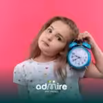 An autistic girl holds a blue alarm clock against a bright pink background, showing curiosity about time and daily routines