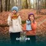 Two autistic kids in warm clothing stand on a forest path covered in autumn leaves, eating apples & enjoying a peaceful time