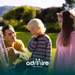 Therapist guides two autistic kids at a sunny park activity board, fostering learning and family‑friendly engagement.