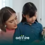 Therapist in pink shirt guides autistic girl playing colorful guitar, both focused and engaged in music.