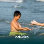 Three autistic children laugh and splash water together while playing in shallow ocean waves on a sunny day at the beach.
