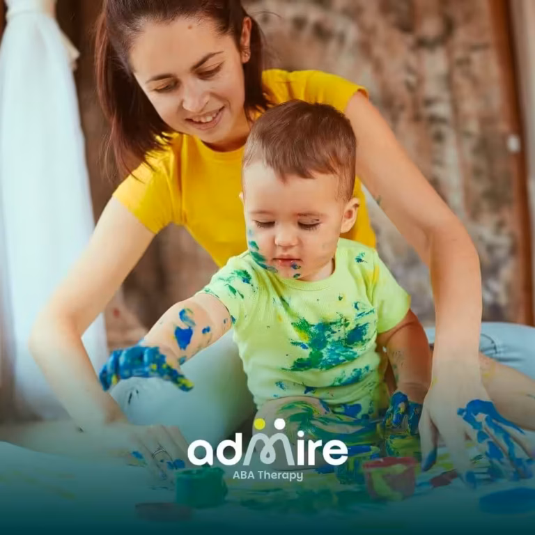 Therapist and autistic toddler painting together on floor, showcasing sensory play and early ABA therapy techniques.