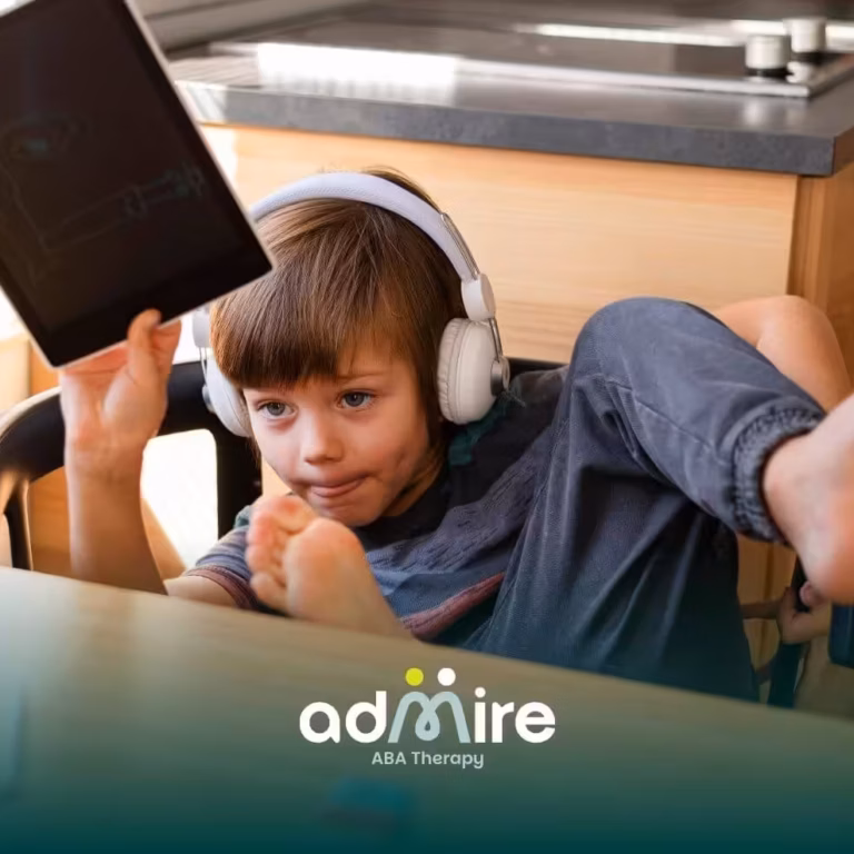 Autistic boy wearing headphones & holding a tablet at a kitchen table, illustrating screen use & modern childhood activities.
