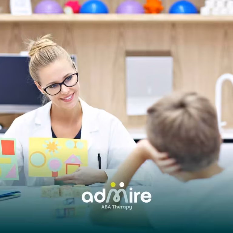 Female therapist showing colorful shape cards to a young autistic boy during an educational therapy session.
