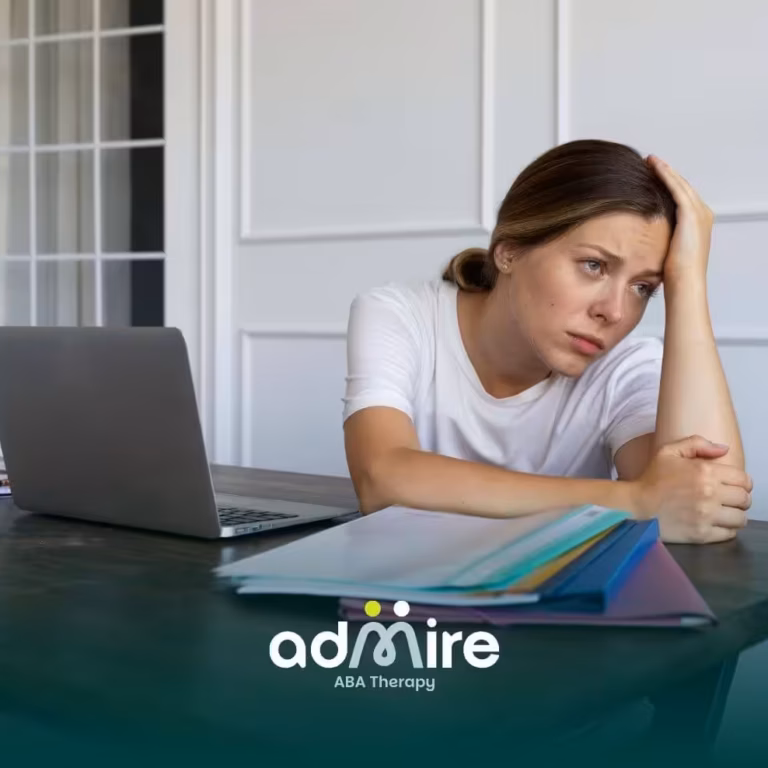 Stressed ABA women sitting at a desk with a laptop and folders, holding her head while worrying about responsibilities.