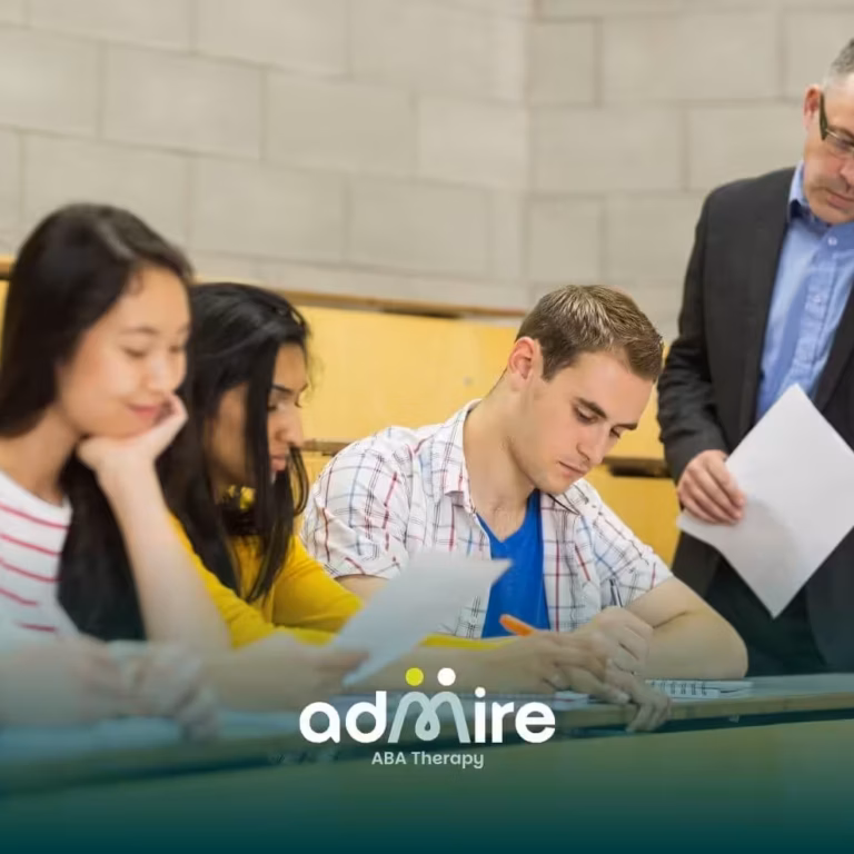 A male therapist observes ABA therapy students writing an exam in a lecture hall classroom environment.