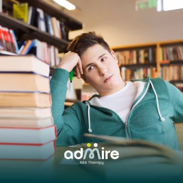 ABA student leaning on his hand in a library surrounded by stacked books, looking overwhelmed while studying.