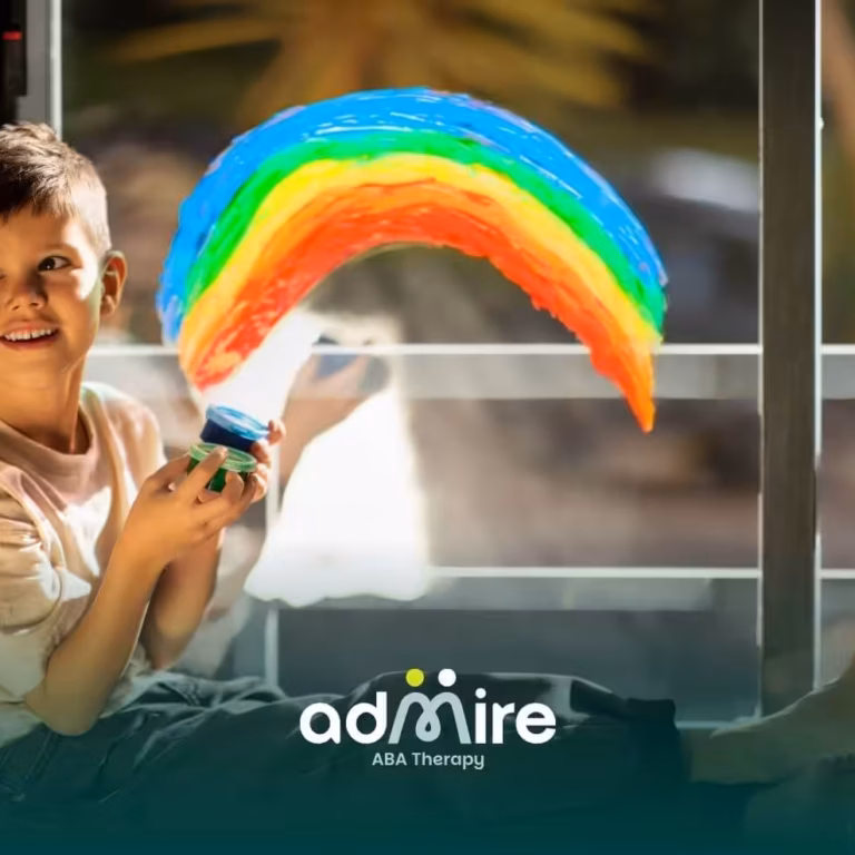 Autistic child sitting by a window painting a colorful rainbow on glass with bright paints during a creative art activity.