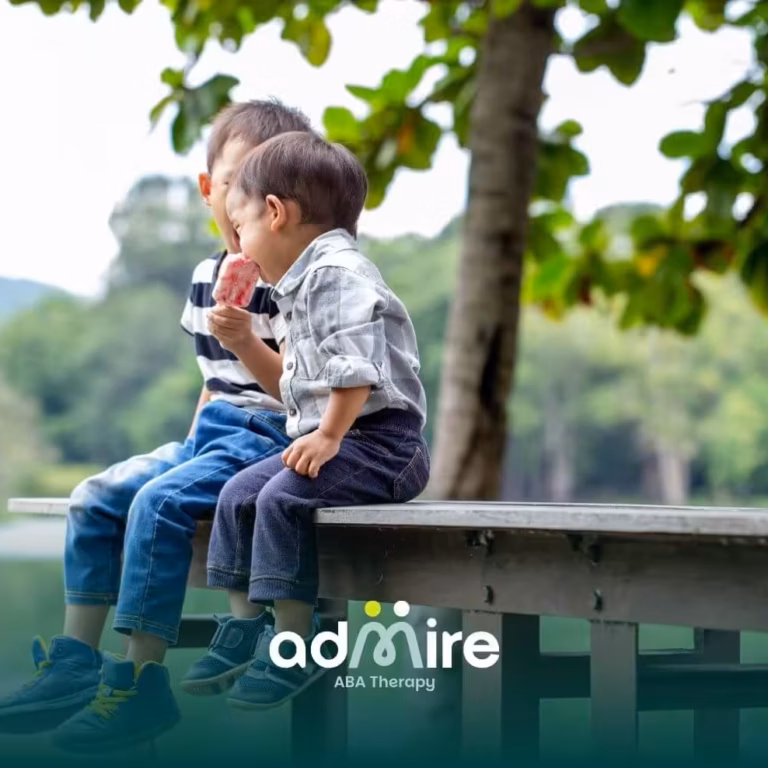Two autistic children sitting on a wooden dock by a lake, sharing a frozen treat and enjoying time together outdoors.
