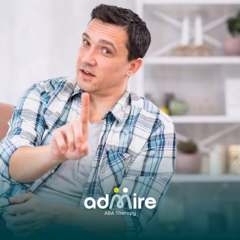 Male therapist sitting in a chair at home, raising his index finger as if explaining or making a point during conversation.