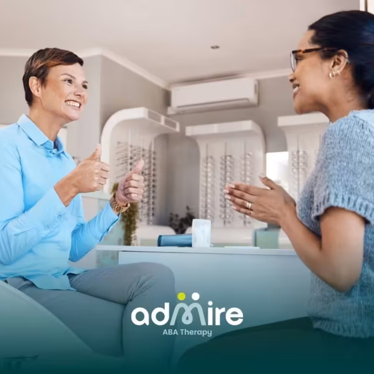 Two therapists communicating using expressive gestures & smiles during a supportive conversation in a bright office setting.